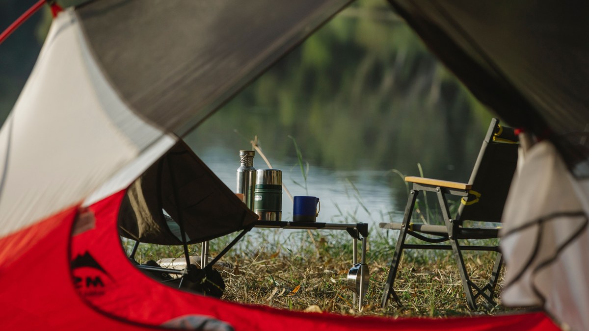 A view from a tent onto a folding table, chairs and a flask