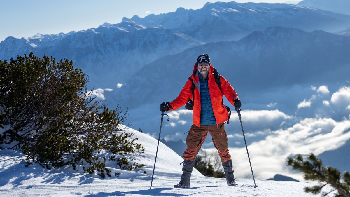 A hiker in a down jacket on a snowy ridge above the clouds