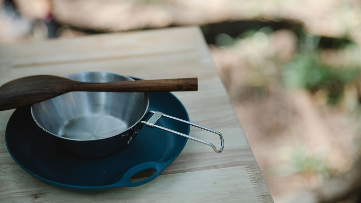 A metal pot and a wooden spatula on a camp table